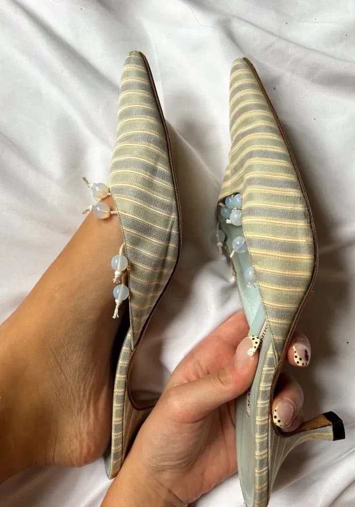 Pale blue and cream striped silk kitten heel mules with glass bead ties, held in a hand