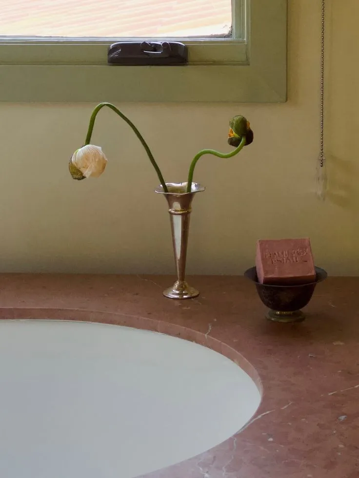 Slim fluted silver vase holding two poppies on a pink marble ledge beside a soap dish